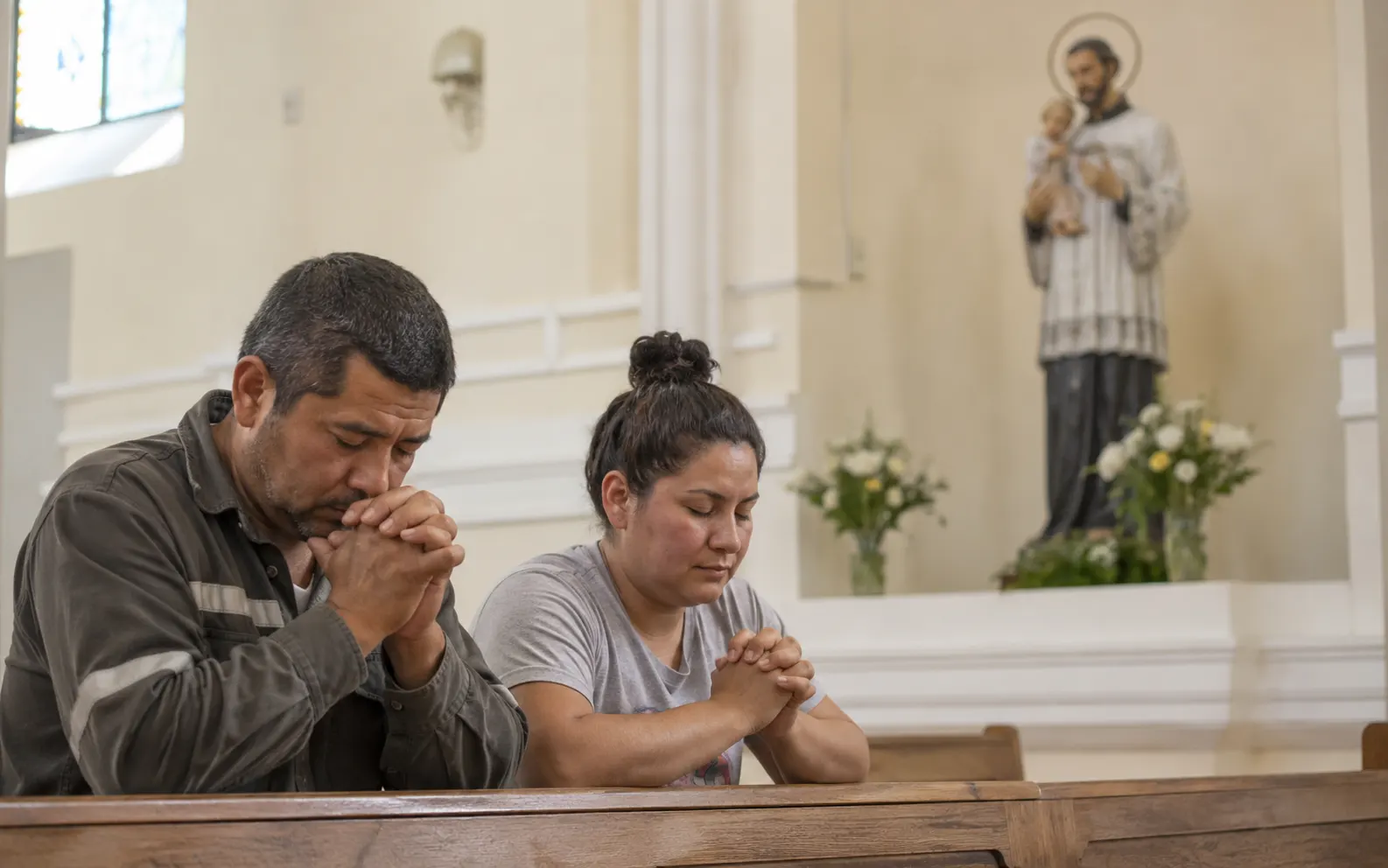 Hombre y mujer rezando en una iglesia durante una oración a San Cayetano